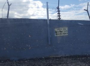 The border fence with the sign declares not to go down from the road to the path on side that used to show tracks of people who crossed the fence