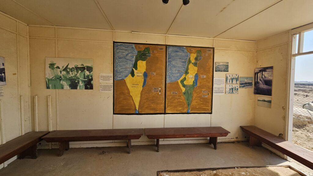 A cabin with the map of the United Nations Partition Plan for Palestine and map of the Peel Commission as well as a table with the water system built here.