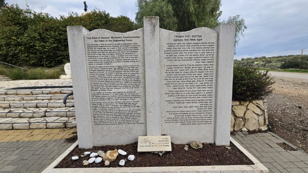 'The Road of Heroism" Monument, Commemorating the Fallen of the Engineering Corps. From December of 1947, the onset of the War of Independence, Arabs
attacked Jewish neighborhoods in Jerusalem and managed to cut the it off from the coastal plain. As a result of their success in blockading the route, the city was under siege, the residents suffered from a severe lack of water, food, fuel and ammunition and rations were distributed.
On the 18 of May 1948, immediately following the declaration of Independence of the State of Israel, a Jordanian force took control of the post at Latrun, thereby blockading the main route to Jerusalem. The situation in the city, which was completely dependent upon the supply convoys that occasionally succeeded in breaking through the worsened.
Following the failure of IDF's attacks on Latrun, a detour route from the south named "The Burma Road", was undertaken in June 1948; after a complex engineering operation a dirt road was paved, through which weapons, food, water and essential equipment from the coastal plain reached the besieged Jerusalem. A book tells about the engineering operation: "When they traveled  to Hulda they found the Brigade Commander in the dining hall. He said to them: " our patrols found a path which by - passes Latrun in the areas under our control. We can pave a route to Jerusalem without the Jordanians or the Egyptians: You will pave the road". They explored the area.,. While under intenise fire night the difficult boulder-filled area was paved. The work continued day and night, boulders were exploded, summits were straightened, and valleys were filled ... And the route was conquered" (from the book "Derekh
Ba'Midbar" (A route in the Desert) by Shlomo Sheba).
A new highway to Jerusalem, which replaced the dirt road was inaugurated on December 7th of 1948, towards the end of the war. This highway, between the Nachshon and the Shimshon intersections, Served the vehicles traveling to Jerusalem until Latrun was conquered in the Six Day War in 1967. It is called "The Road of Herolsm".
The monument before you was dedicated to the pavers of the route during 
the War of Independence. The central stone pillar with the passage "If I forget thee, O Jerusalem", was inaugurated in 1950. In 1982 the memorial site was declared the central site for the fallen soldiers of the Israeli Engineering Corps.
The Engineering Corps belong to the ground forces and are in charge of mine laying and demolition, overcoming natural and man made obstacles and operating mechanical engineering equipment. Heavy and light light equipment is is used in the Engineering Corps for carrying out the different missions such as  blowing up mines, filling channels, breaking through routes in difficult terrain and creating ground obstacles. Upon changing the monument to be centeral meorial site for the engineering corps, the area of the square was widened, and walls  containing and commemorating the names of the fallen soldiers were added.